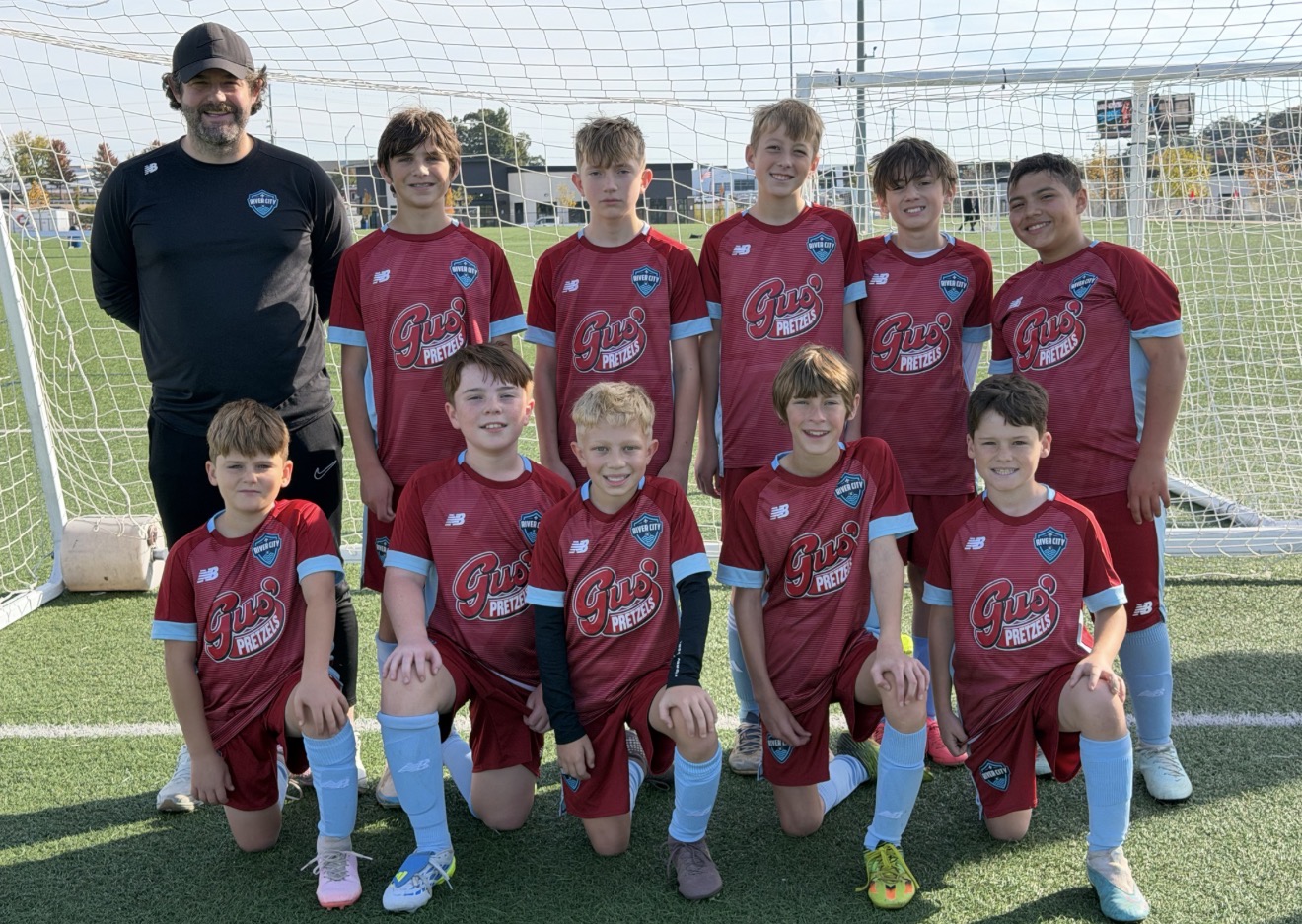 River City FC boys team in maroon kits with their coach in front of a soccer goal